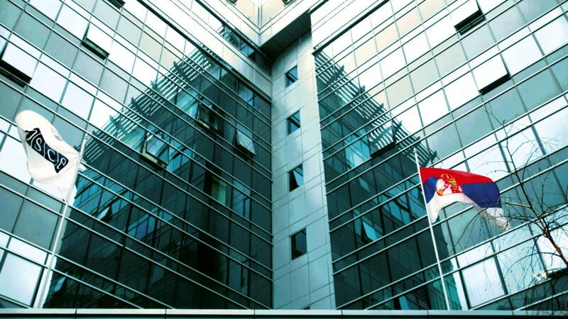 Glass building exterior reflecting sky, with two flags on poles.