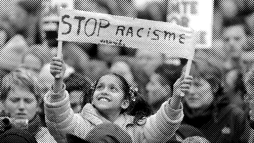 Smiling child in a blue coat holds a "Stop Racisme" sign at a crowded protest.