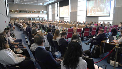 Large conference room filled with seated attendees, facing a presentation screen.
