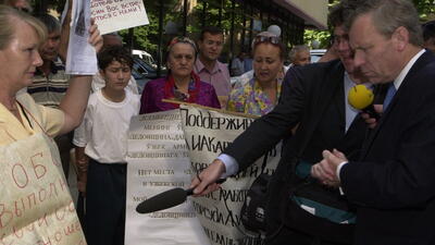 The Netherlands foreign minister in 2003, Jaap de Hoop Scheffer, looks at posters held up by protesters while a journalist with a microphone in his hand points at the posters to translate their meaning.