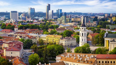 Skyline of Vilnius with colorful historic buildings, lush green trees, and modern skyscrapers under a blue sky.