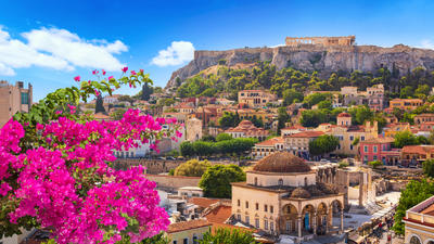Athens cityscape with vibrant pink flowers, historic buildings, and the Acropolis perched on a hill under a clear blue sky.